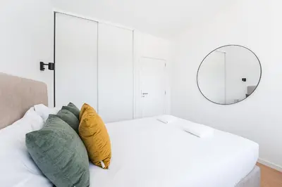 a white bedroom with a bed with pillows and a mirror at GuestReady - Casa da Música Cosmopolitan Comfort in Porto