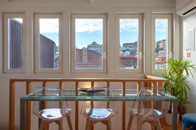 a glass table and two stools in a room with windows at Mouzinho Rooftop View in Porto