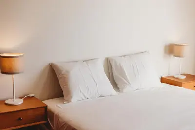 a bed with white sheets and pillows and two lamps at Apartamento Santos Pousada 2 in Porto