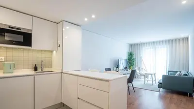 a kitchen with white cabinets and a living room at Serene 1BR Spot by LovelyStay in Porto
