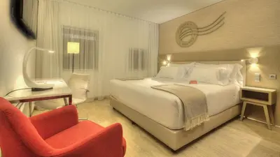 a hotel room with a bed and a red chair at NH Collection Porto Batalha in Porto
