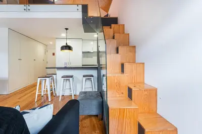 a living room with a staircase and a kitchen with stools at GuestReady - Charming Mezzanine near Porto in Vila Nova de Gaia