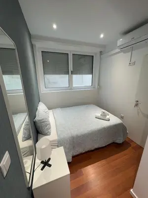 a small bedroom with a bed and two windows at Dormitório Aliados in Porto