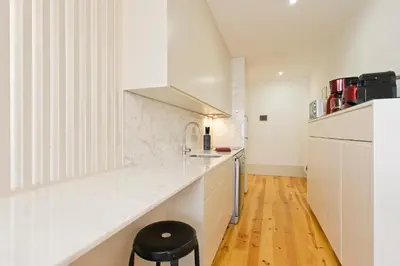 a white kitchen with a counter and a stool at Aposentus - Premium Central Apartment 1BR in Porto