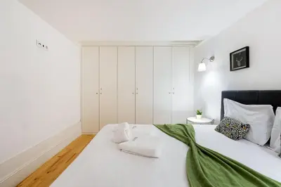 a white bedroom with a large bed with a green blanket at GuestReady - Dolce experience in Porto in Porto