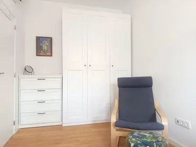 a white bedroom with a blue chair and a dresser at Charming Campanhã Family Home in Porto