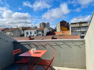 a red table and chairs on a balcony with a city at Sunny rooftop duplex with elevator near iconic bridge in Vila Nova de Gaia