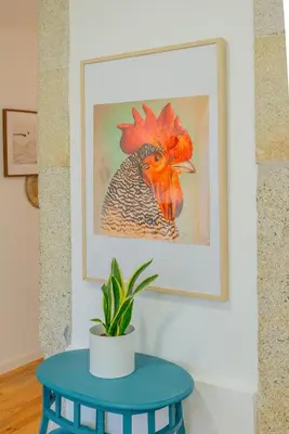 a painting of a rooster on a wall with a blue table at VIVA República Serviced Apartment in Porto