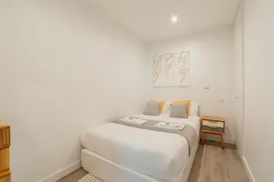 a white bedroom with a bed and a chair at Downtown Cosy Apartment by Vacationy in Porto