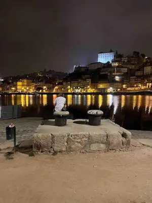 a person sitting on a bench by the water at night at Art Wine Loft with oPorto view! in Vila Nova de Gaia