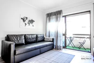 a black leather couch in a living room with a window at 2Bedroom Flat - Families, remote work, downtown - Private Garage in Porto