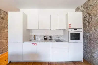 a white kitchen with white cabinets and a stone wall at Vila Rio Guest House in Vila Nova de Gaia