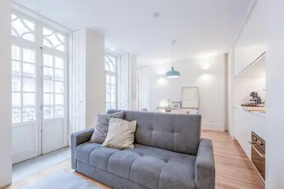 a living room with a gray couch and some windows at Modern Flat With Balcony on Rua das Flores - 1st in Porto
