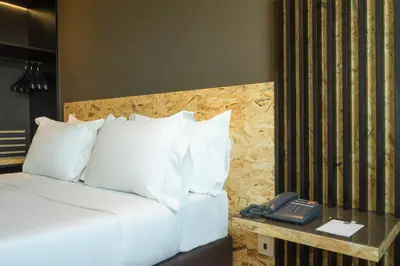 a bed with white pillows and a phone on a table at HF Ala Sul in Porto
