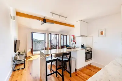 a kitchen with white cabinets and a counter with a table at Sol Do Porto - 2 bed Penthouse Luis Bridge view in Porto