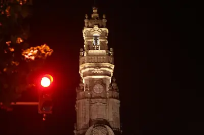 a clock tower at night with a red traffic light at 2U Oporto Urban Stays in Porto