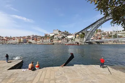 a group of people sitting on the banks of a river with a bridge at FLH Porto Stylish Apartment in Porto