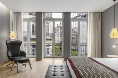 a bedroom with a bed and a chair and large windows at Eurostars Porto Centro in Porto