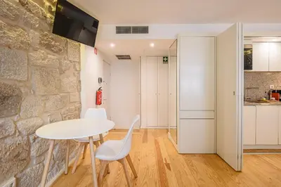 a white table and chairs in a room with a stone wall at PWHC Miragaia Apartments in Porto