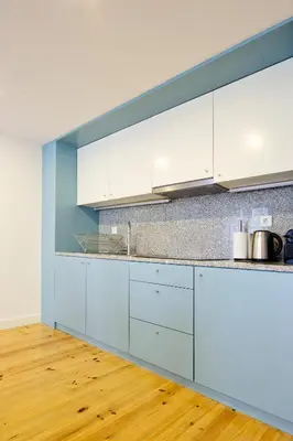 a kitchen with white cabinets and a wooden floor at Oliveirinhas Porto Apartment in Porto