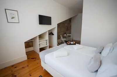 a white bedroom with a large bed and a television at Turista Da Trindade in Porto