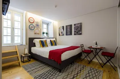 a bedroom with a bed and a table and two windows at Virtudes City Lofts in Porto