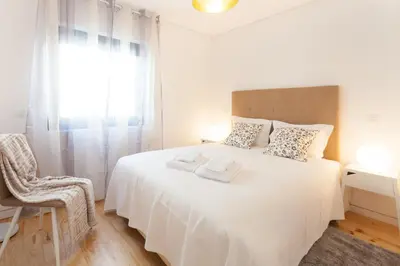 a bedroom with a white bed with a chair and a window at Urban Views Townhouse Arrábida in Porto