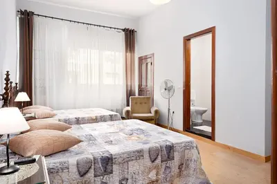 a bedroom with two beds and a chair and a mirror at Almada Guest House in Porto