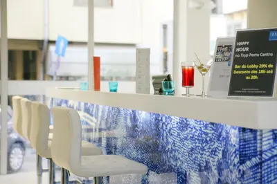 a bar with white chairs and a counter with a drink at TRYP by Wyndham Porto Centro Hotel in Porto