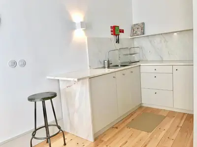 a white kitchen with a counter and a stool at Lóios Flat in Porto
