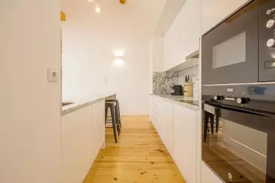 a kitchen with white cabinets and a wooden floor at Loft D. João IV in Porto
