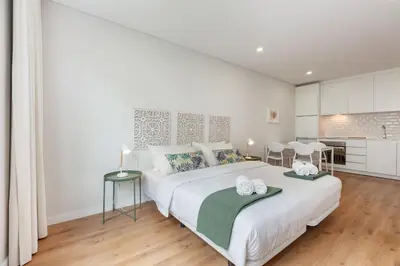 a white bedroom with a large white bed and a kitchen at Oporto Palace Apartments in Porto
