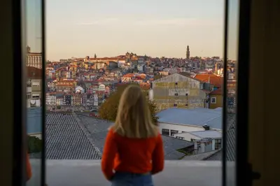 a woman looking out of a window at a city at Feel Porto Wine Essence Apartments in Vila Nova de Gaia