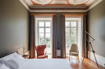 a bedroom with a bed and two chairs and windows at Menina Colina Guesthouse in Porto