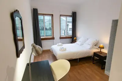 a bedroom with a bed and a table and two windows at Change The World Hostels - Porto - Santa Catarina in Porto