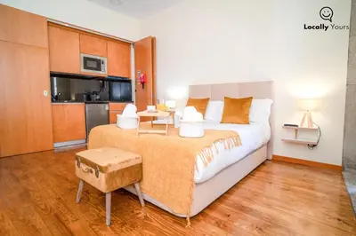 a bedroom with a large bed and a kitchen at Locally Yours Oporto Apartments in Porto