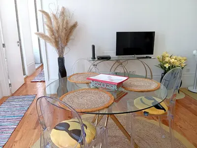 a glass table with four chairs and a television at Appartement Pont Luiz in Porto