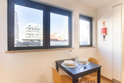 a dining room with a table and two windows at Homely Studio w/ AC near Marquês by LovelyStay in Porto