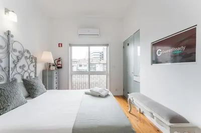 a white bedroom with a large bed and a tv at GuestReady - Gold Leaf in Porto