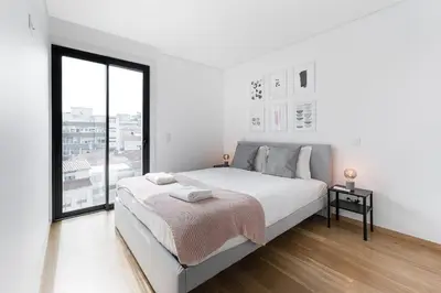 a white bedroom with a bed and a large window at GuestReady - Poet's Modern Retreat in Porto