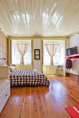 a bedroom with a bed and wooden floors and windows at Porto Sé Apartamentos in Porto