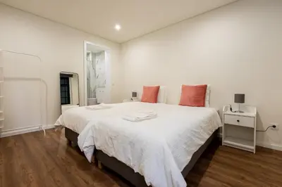 a white bedroom with a large white bed with red pillows at Entire House with 4 Master Suites, Hot Tub & Backyard - Central Location in Vila Nova de Gaia