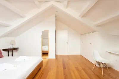 a white bedroom with a white bed and a chair at Apartamentos da Capela in Porto