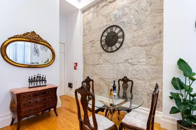 a dining room with a glass table and a stone wall at Majestic Cafe - Porto City Center Modern Apartment in Porto
