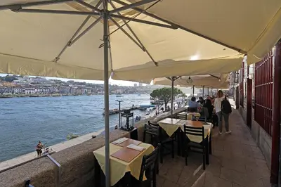 a restaurant with tables and umbrellas next to a river at FLH Porto Ribeira with River View in Porto