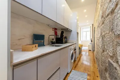 a kitchen with white cabinets and a stone wall at A Window to Porto - Premium apartment by the River in Porto