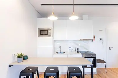 a kitchen with white cabinets and a table with stools at Wonderful Duplex W Private Patio & AC by LovelyStay in Porto