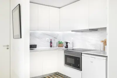 a white kitchen with white cabinets and a black microwave at República Garden View in Porto