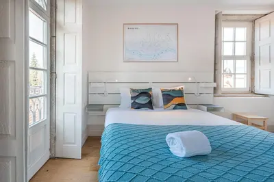 a bedroom with a bed with a blue comforter and two windows at GuestReady - Porto Wine District Penthouse in Vila Nova de Gaia